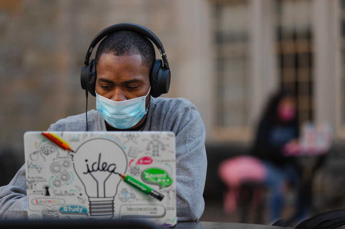 Masked man with headphones using a laptop.