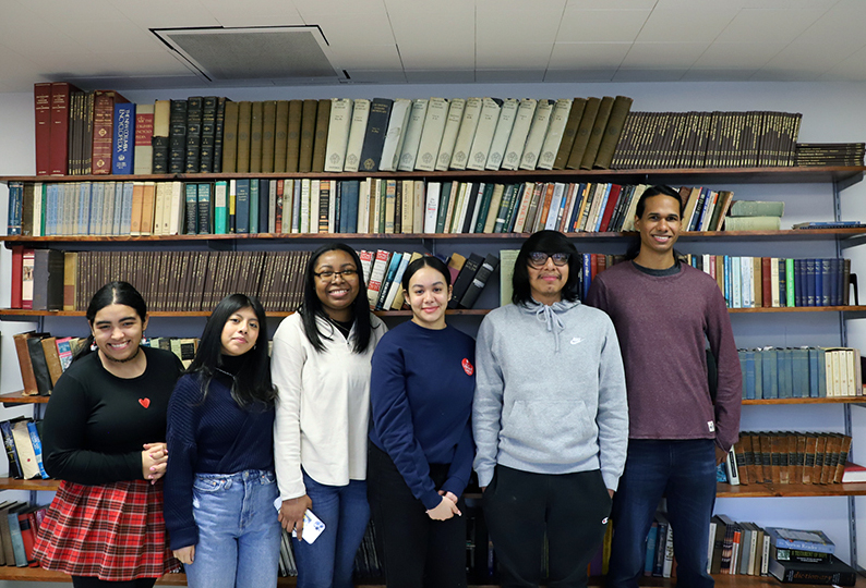 A group of students standing in front of a bookshelf.