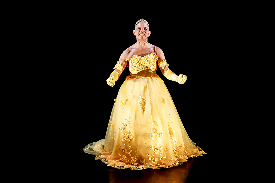 Artistic portrait of a man in a yellow ball gown against a black background.