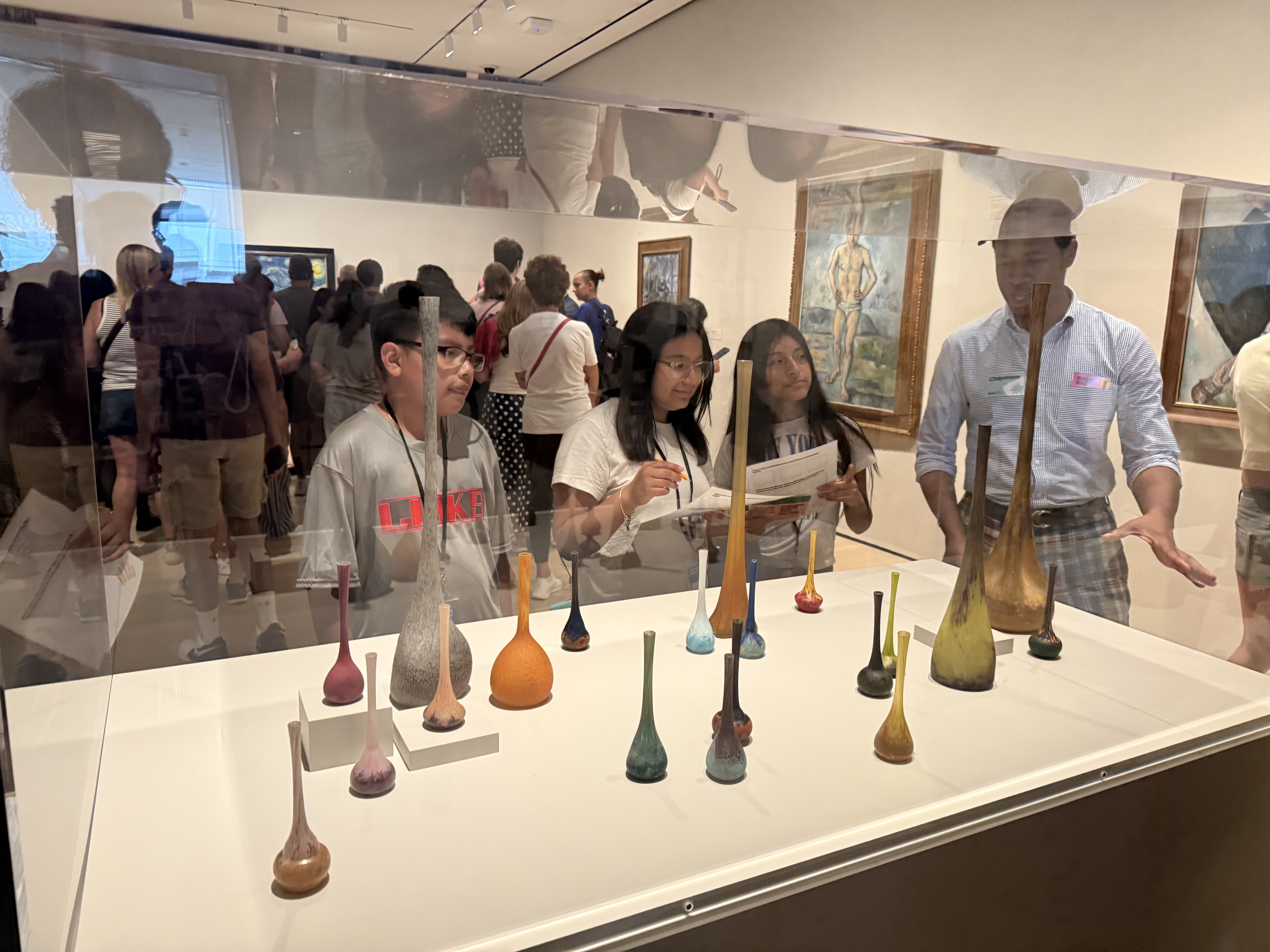 Students in a museum gallery looking at a vitrine displaying glass vases.