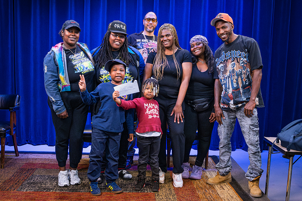 Six adults and two children on a stage celebrating their win.