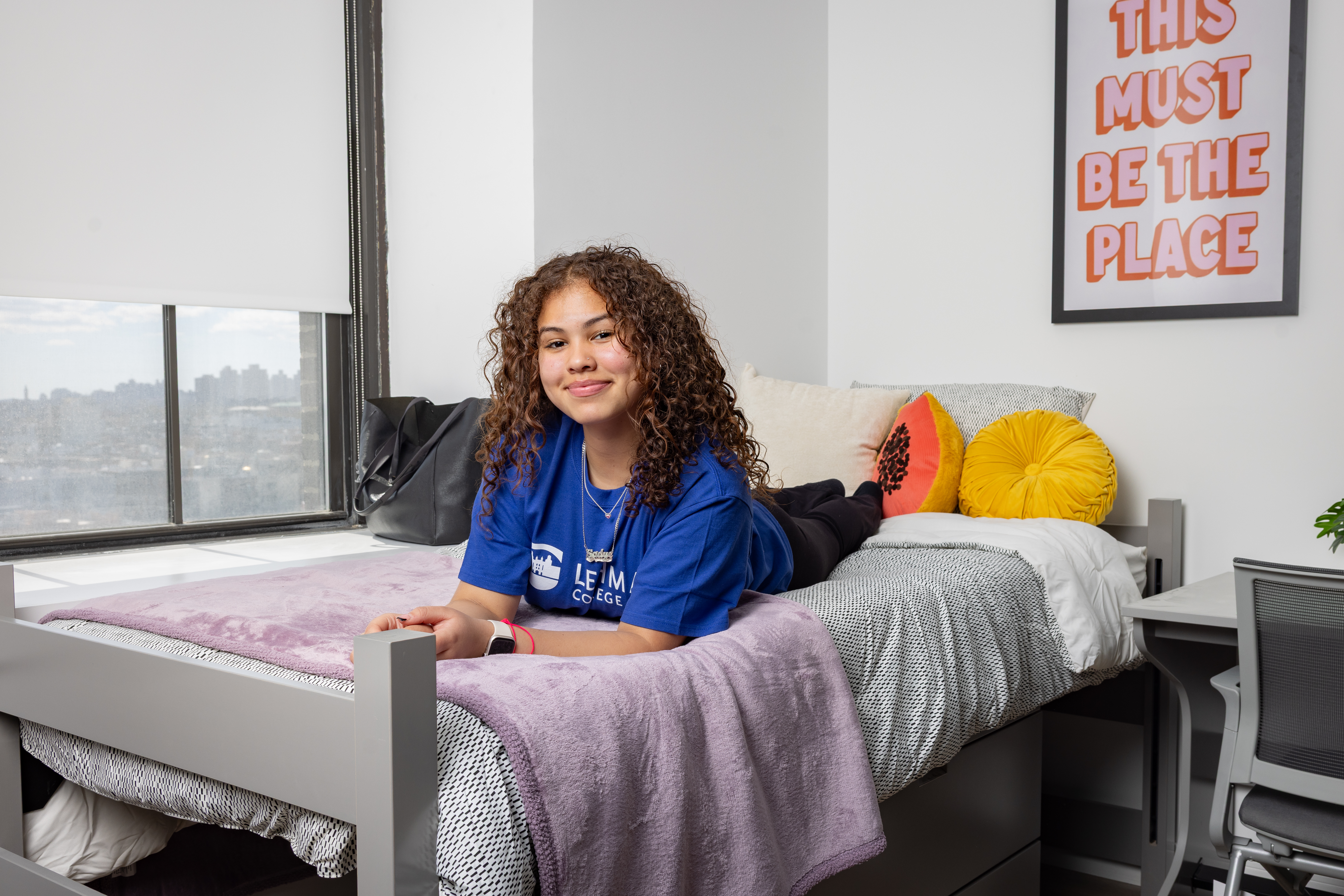 A student on a bed in a Lehman Grand dorm room.