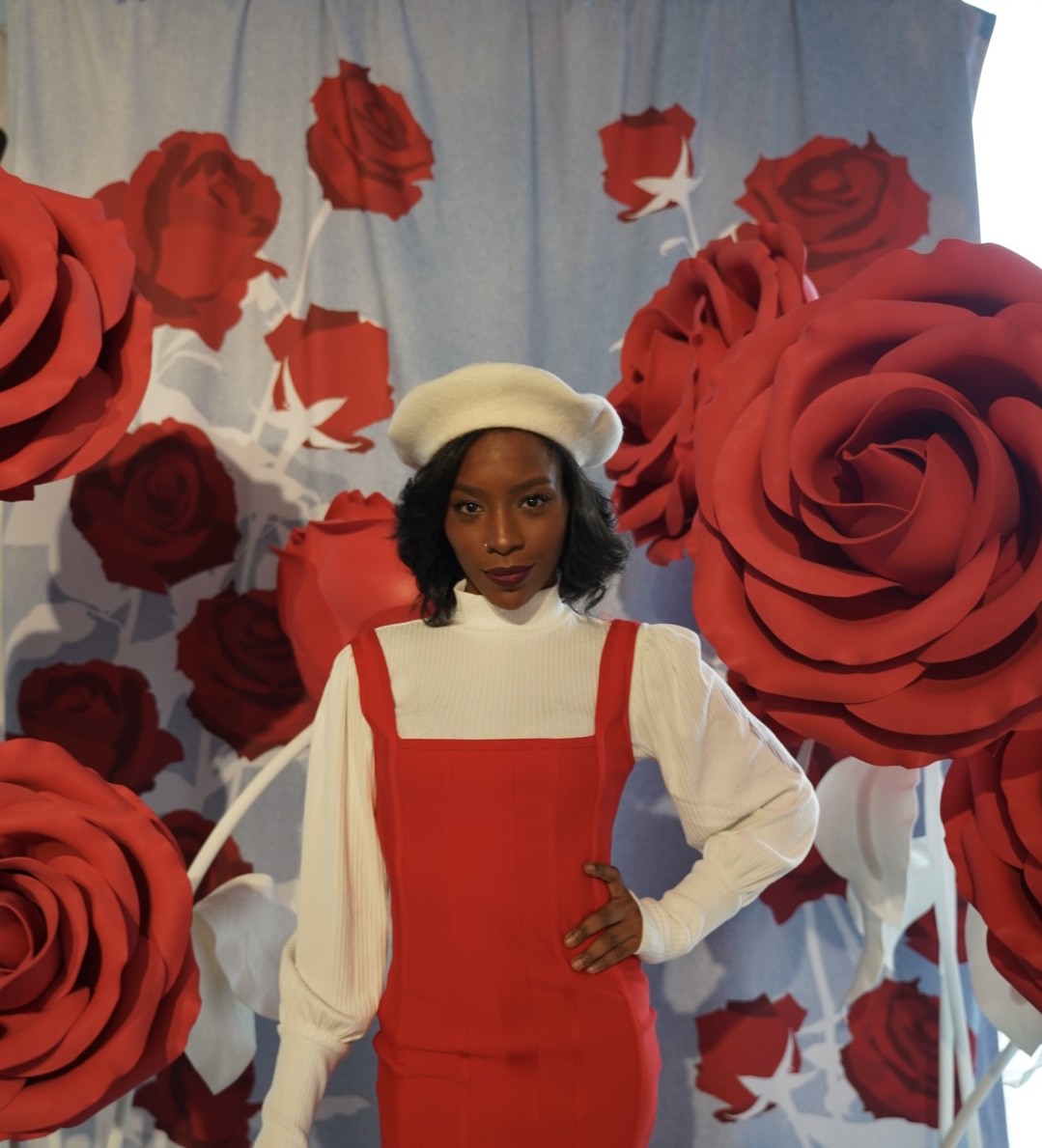 Porshe Maysonet posing in a red dress with large decorative roses hanging around her.