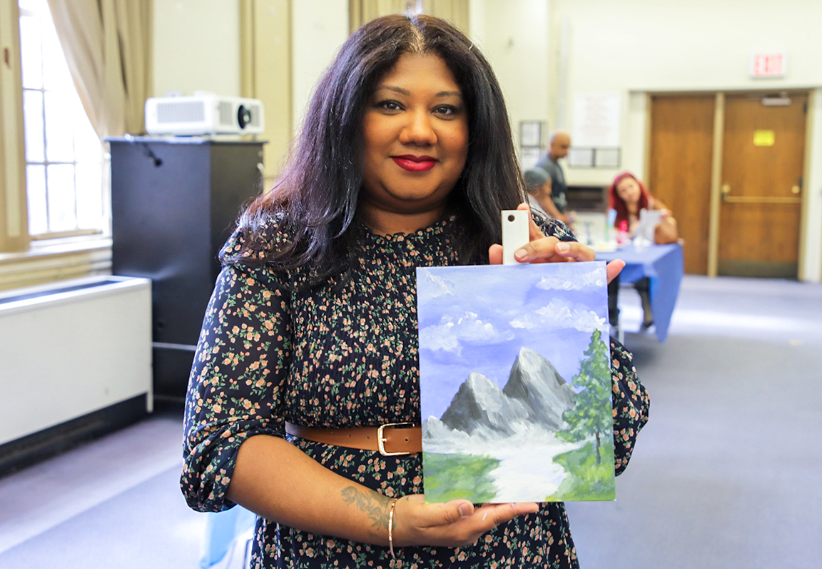 Christine Sohan holding a painting of mountains and a pretty backdrop