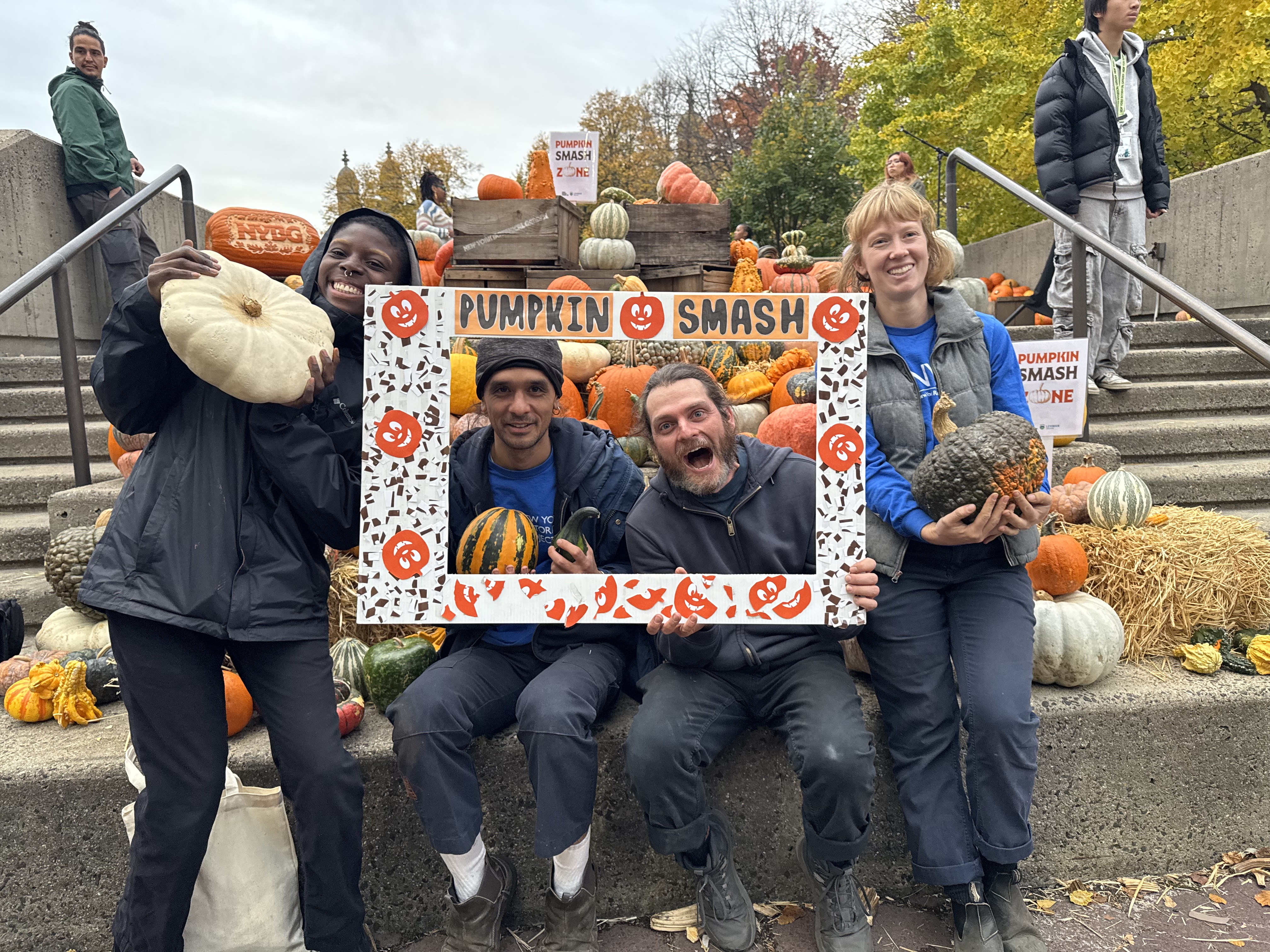 A group of adults holding a large decorative photo frame around their faces that says 'pumpkin smash.'
