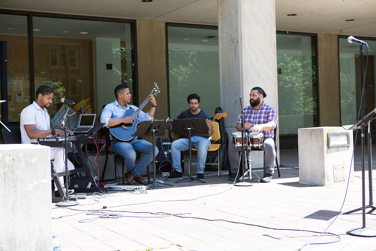 Live outdoor band performance with a keyboardist, guitarist, bassist, and bongo player.