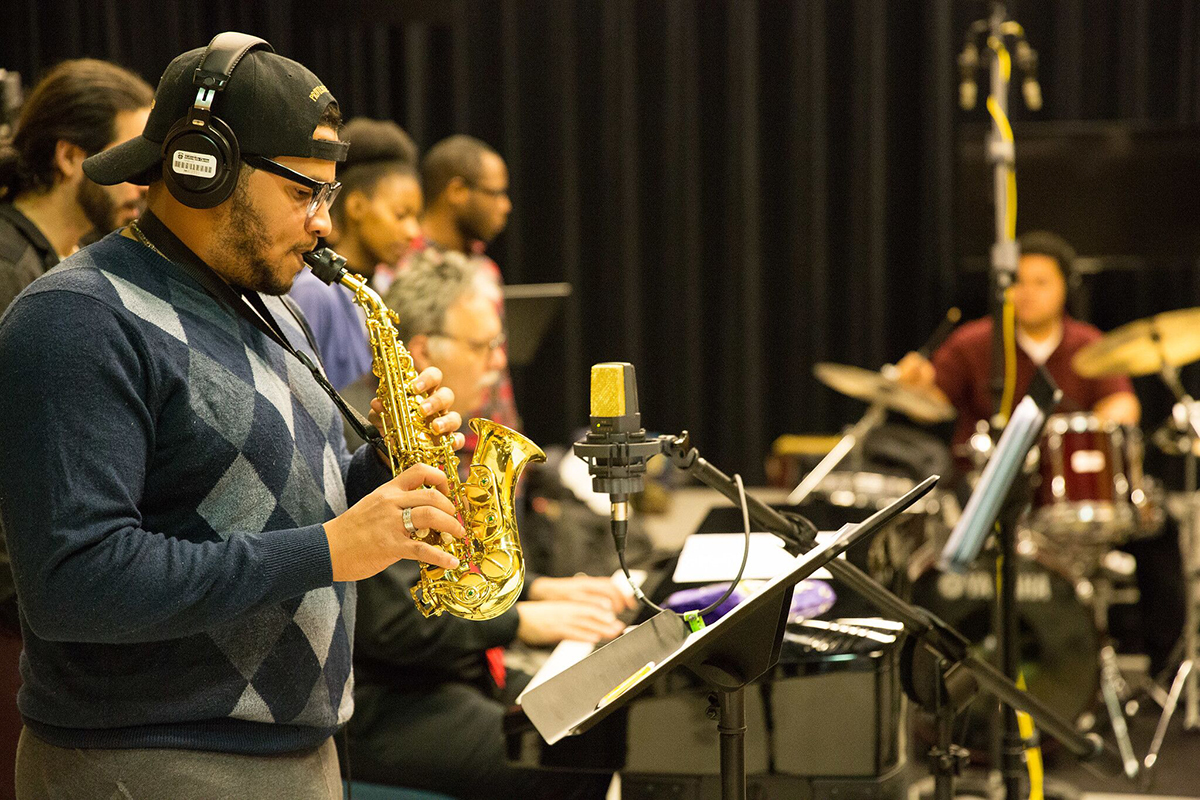 Saxophonist wearing headphones performing with a band in a recording studio.