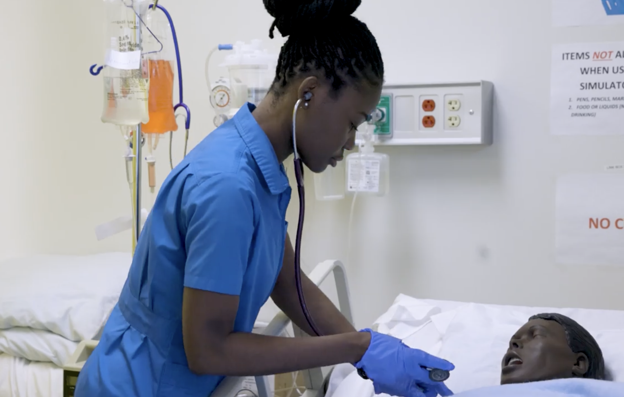 Catherine wearing blue nursing scrubs and working with a mannequin
